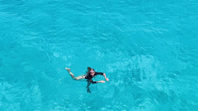 A teenage girl in a black swimsuit swims in a Mediterranean lagoon with crystal-clear turquoise water. Summer vacations, active leisure, adventure travel, and seaside recreation.