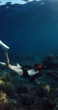 Woman swims underwater in transparent clear ocean over coral reef in Raja Ampat