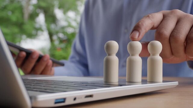 Human Resources department choosing wooden figurine while using a smartphone and laptop to represent digital online recruitment. decision-making in recruitment and choosing the right talent