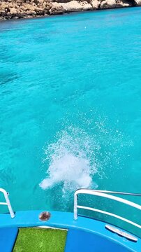 Teenage girl jumps from a tour boat into the crystal clear turquoise Mediterranean Sea. Summer vacation adventure, active leisure and travel experience in a beautiful coastal destination.