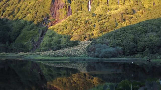 At golden hour, drone glides past taro leaves toward cascade-laced cliffs cinematic opener, Flores, Azores