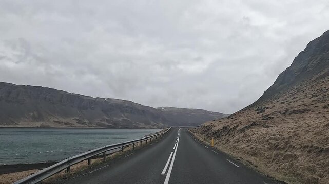 Dashboard POV on Route 47 hugging Hvalfjordur shoreline between steep mountain walls, West Iceland, Iceland