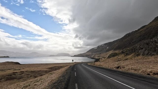 Scenic Route 47 along Hvalfjordur fjord with steep snow-patched mountains and calm water, West Iceland