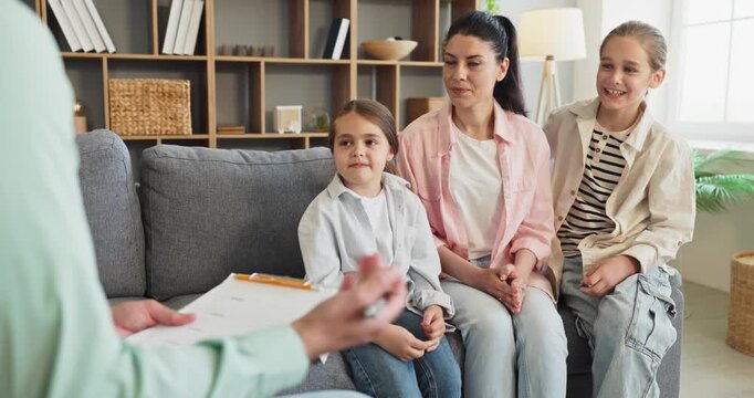 Family counseling therapy with mother and children. They sit on a sofa during a supportive session discussing communication and emotions with a therapist. Strong family support concept.