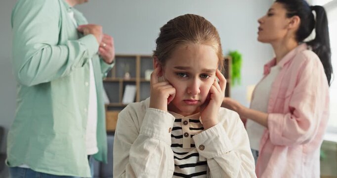 Child parents argument conflict family home stress fear. Distressed girl covers ears as parents argue loudly, feeling overwhelmed and anxious in the livingroom. Clear theme is family conflict.