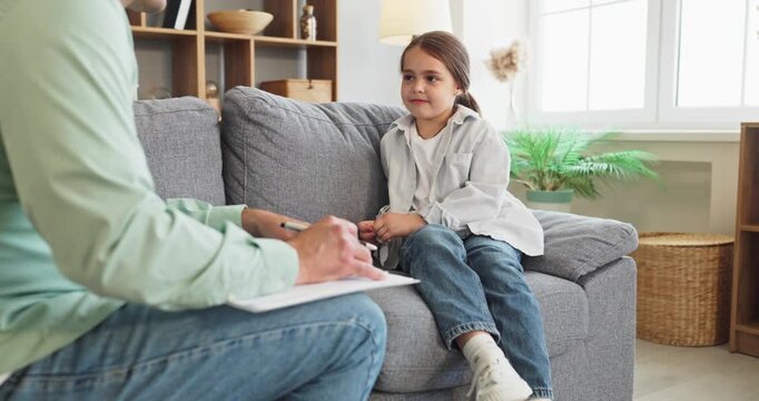 Child psychologist therapist counseling therapy session conversation. Girl on sofa as therapist notes, offering consultation and reassurance. Clear child therapy support concept today.