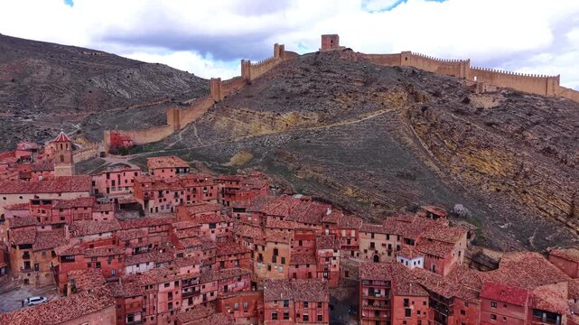 Well-preserved medieval fortress walls crown a rocky ridge above Albarracin's pink-hued terracotta rooftop village with church tower, Teruel, Aragon, Spain