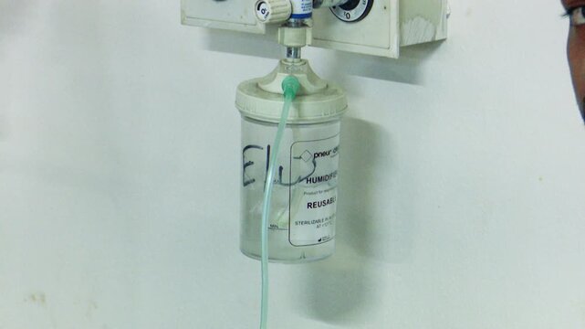 Medical oxygen cylinder with regulator and flow meter mounted on hospital wall for respiratory patient care