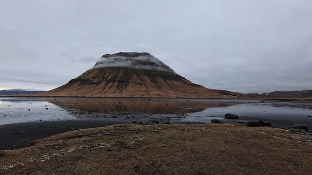 Kirkjufell flat-topped peak with low cloud reflected in still tidal flats at dusk, Grundarfjordur, Iceland
