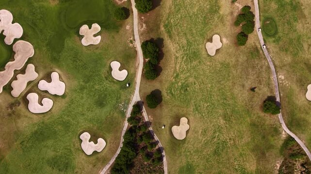 Overhead view of a golf course fairway in Spain featuring irregular white sand bunkers, winding cart paths, scattered trees, and green grass creating an abstract geometric pattern
