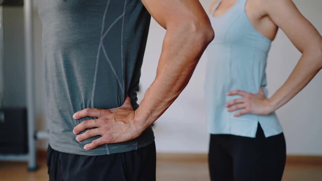 Starting upright hands on hips, pair performing backbend for mobility in gym, grey blue tops, cable