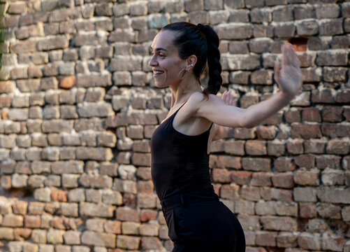 Beautiful young Hispanic woman dancing in black tank top and pants against brick wall. Urban street dancer.