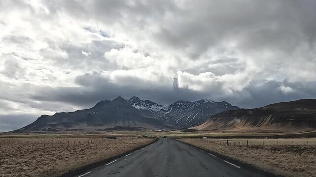 Dashboard POV on Snaefellsnes Peninsula road, dramatic Snaefellsjokull glacier and jagged peaks under storm sky