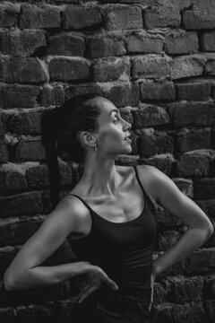 Black and white portrait of sweaty Hispanic woman with fit toned body and defined muscles against brick wall.