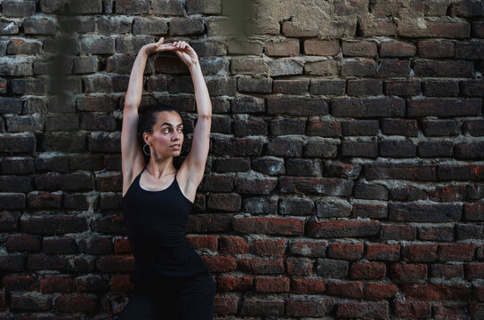 Beautiful young Hispanic woman practicing choreography poses against brick wall. Urban dancer concept.