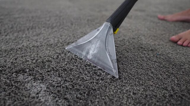 Clear extraction nozzle removing foamy soil from gray carpet with strong suction, visible fiber agitation, wet streaks, swirling solution, and close low angle detail for professional surface cleaning