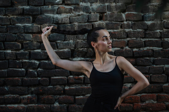 Beautiful young Hispanic woman holding her long braid and looking away against brick wall.