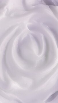 White Cream Swirling. Thick glossy cream moves in smooth folds, creating a soft abstract cosmetic texture.