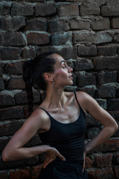 Medium shot of beautiful young Hispanic woman showcasing fit body and glowing skin against brick wall.