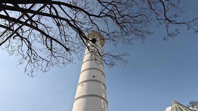 Dharahara tower in Basantapur, Kathmandu, dolly-in looking up the white column through bare branches