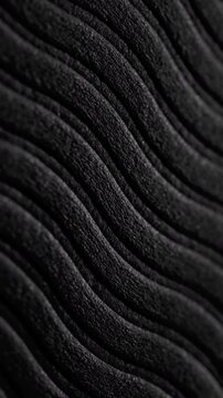 Black wavy ribbed texture slow pan. Close-up of deep black textured surface with vertical wavy ridges. Smooth linear camera movement reveals shifting light and shadow across the pattern.