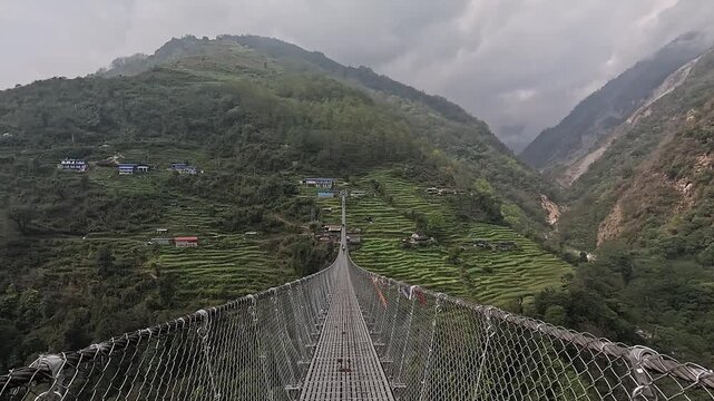 Dolly toward the towering Jhinu Danda suspension bridge over green terraces and village, Annapurna Base Camp trek, Nepal