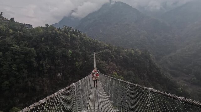 Porter carries a heavy load across the Jhinu Danda suspension bridge high above the valley, Annapurna Base Camp trek, Nepal