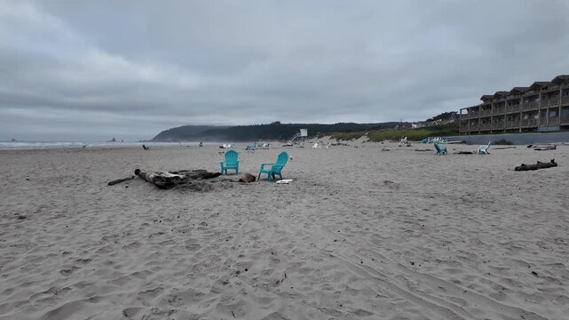 4K smooth stabilized footage of empty Adirondack chairs on Cannon Beach after Independence Day celebrations with Haystack Rock, Pacific Ocean and cloudy summer sunrise in Oregon, USA
