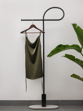 Elegant  satin slip dress hanging on minimalist clothing rack with tropical plant