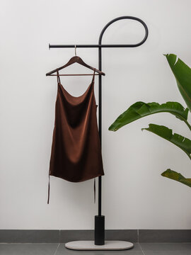 Elegant  satin slip dress hanging on minimalist clothing rack with tropical plant