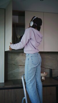 Woman cleans kitchen cabinet while standing on a step stool in a modern kitchen