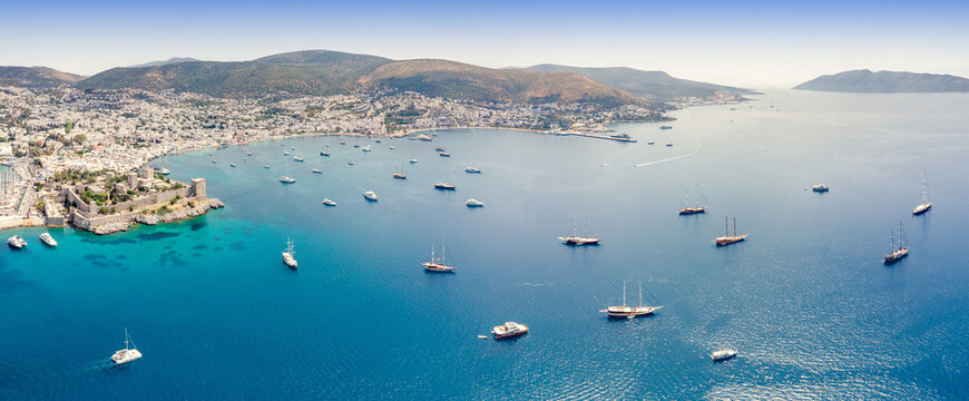 Bodrum Peninsula coastline with historic castle and numerous boats anchored in the clear turquoise waters, a vibrant tourist destination