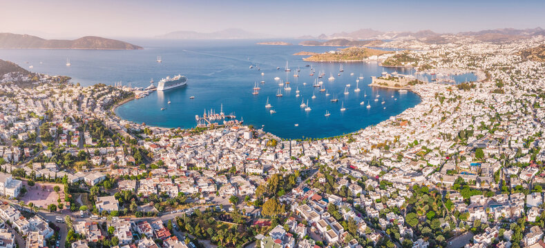 Aerial panoramic view showing Bodrum Castle, many yachts in the marina, and city buildings along the Aegean Sea coast of Turkiye