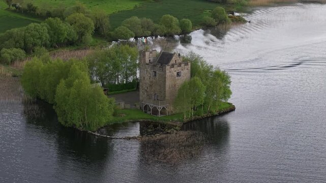 Aerial view of historic stone tower on small island surrounded by calm lake waters