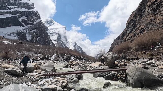Trekkers cross a steel plank bridge over the glacial Modi Khola below snow peaks, Annapurna, Nepal