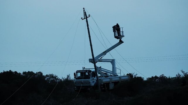 Electrical service men in a crane basket being lifted to fix damaged wires on an electrical line