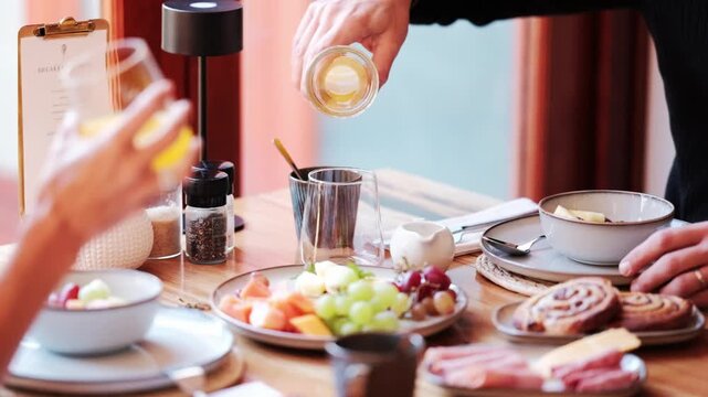 A couple enjoys a breakfast spread while pouring and drinking orange juice