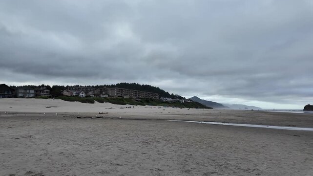 4K smooth stabilized footage of almost empty Cannon Beach with a few distant visitors enjoying a peaceful cloudy summer morning by the Pacific Ocean at sunrise in Oregon, USA