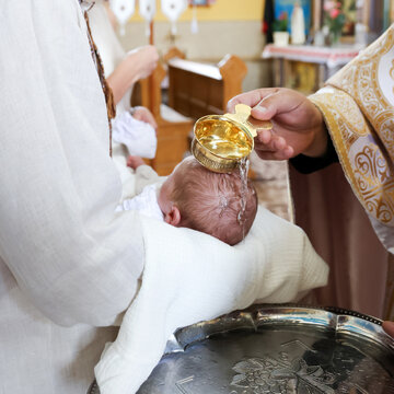 Priest pours holy water over a baby's head during an Orthodox baptism ceremony inside a church.