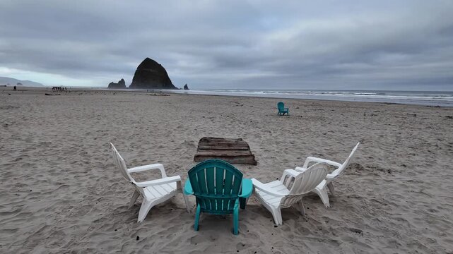 4K smooth stabilized footage of empty Adirondack chairs on Cannon Beach after Independence Day celebrations with Haystack Rock, Pacific Ocean and cloudy summer sunrise in Oregon, USA