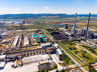 Naklejka premium Industrial site with multiple structures and large water tanks located near a river in a dry area during daytime