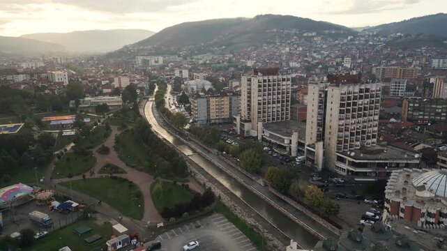 Smooth pulling-back drone shot reveals the panoramic view of Novi Pazar beneath a golden twilight sky, southwestern Serbia.