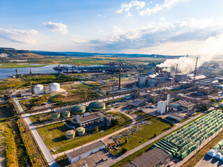 Fototapeta premium Plant and industrial area with storage tanks and factories near a river during the day with clouds in the sky