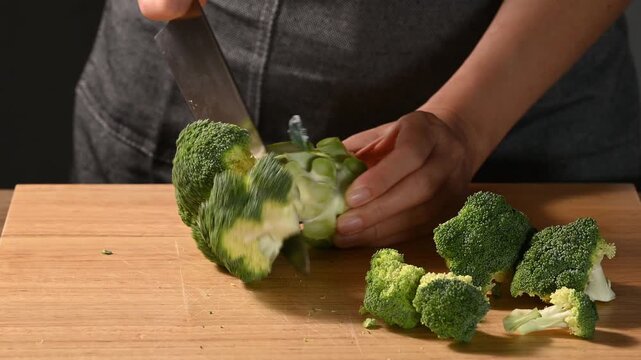 Close-up of woman hand using knife to chopping fresh broccoli on wooden cutting board, meal prep