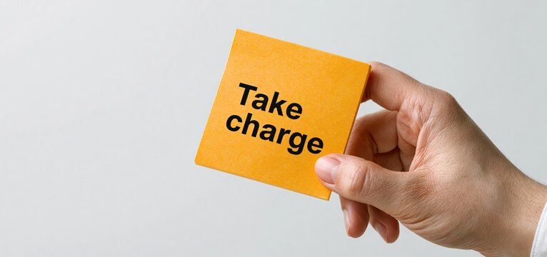 A vibrant orange sticky note with "Take Charge" message held against a plain white backdrop, inspiring empowerment and motivation.
