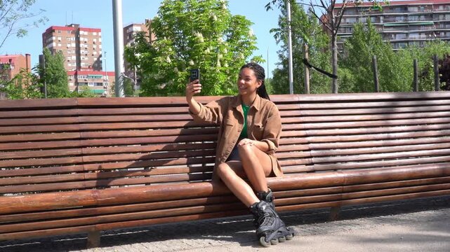 Young woman in rollerblades taking a selfie in the park