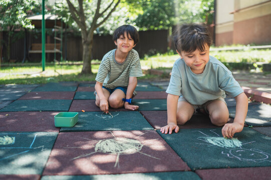 Brothers draw pictures with chalk on the outdoor playground