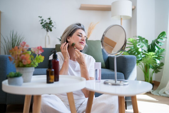 Woman using jade roller for facial care in living room wellness routine