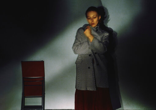 A woman wearing a tweed jacket stands in cinematic shadow