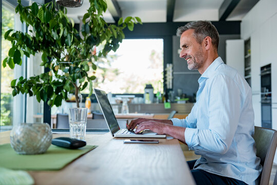 Smiling mature man at home using a laptop at table